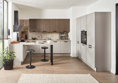 Moderne Häcker Küche mit Fronten in Holzoptik und heller Arbeitsplatte sowie Halbinsel mit Sitzplätzen.
